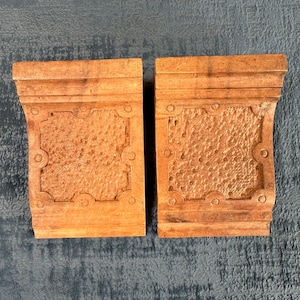 Peut inclure: Deux serre-livres en bois avec un motif décoratif. Les serre-livres sont de couleur brun clair et ont une surface texturée.