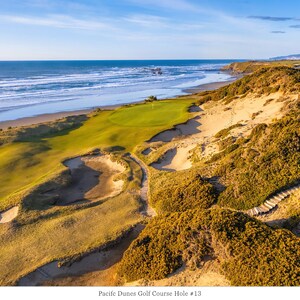 May include: Aerial view of a golf course hole with green grass, sand dunes, and a blue ocean in the background. The hole is number 13 and has a par of 4. The text "Pacific Dunes Golf Course Hole # 13" and "Par 4 - 444 Yards" is visible in the image.