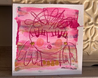 Może przedstawiać: Aquarela w kolorze różowym i złotym przedstawiająca stylizowaną twarz z dużymi oczami i koroną. Podpis artystki "Caroline Crowley" znajduje się w prawym dolnym rogu.