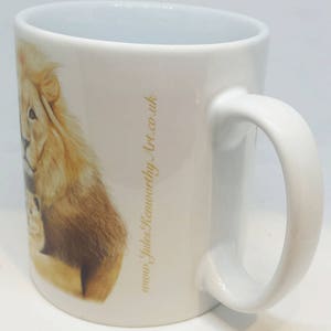 May include: White ceramic mug with a lion and cub illustration. The mug has a gold inscription that reads "www.judes&worthy.art.co.uk".