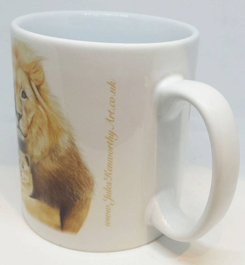 May include: White ceramic mug with a lion and cub illustration. The mug has a gold inscription that reads "www.judes&worthy.art.co.uk".