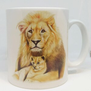May include: White ceramic mug with a colorful illustration of a lion and a lion cub. The lion has a light brown mane and the cub is light brown with a white belly.