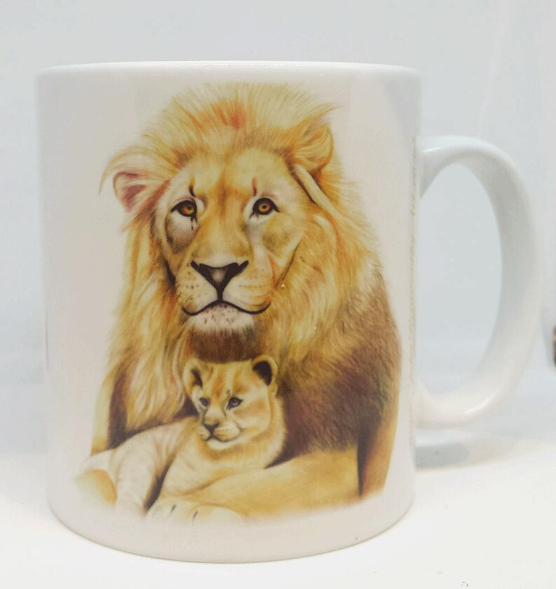 May include: White ceramic mug with a colorful illustration of a lion and a lion cub. The lion has a light brown mane and the cub is light brown with a white belly.