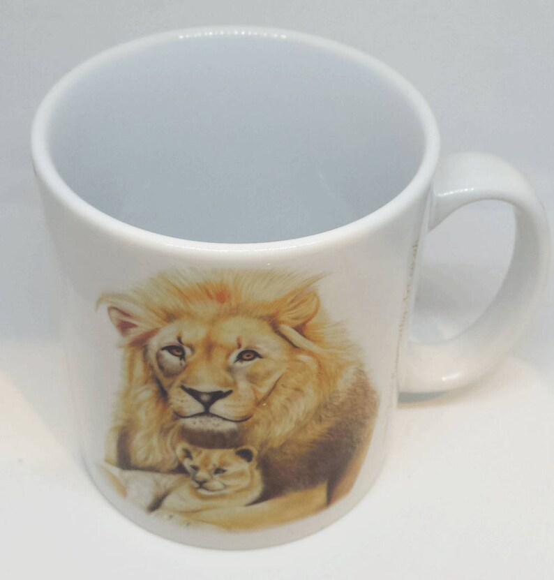 May include: White ceramic mug with a brown and white image of a lion and a lion cub. The lion is looking directly at the viewer.
