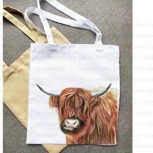 May include: A white tote bag with a brown and white Highland cow illustration. The bag has the text "Jules Kenworthy Art" repeated on the front.