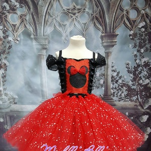 Può includere: Abito tutu rosso e nero con un designo di Minnie Mouse nero e rosso sul corpetto. L'abito ha una gonna di tulle rosso scintillante e un bordo di pizzo nero sul corpetto. L'abito è su un manichino bianco.