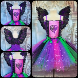 May include: A multi-colored tutu dress with a pink bodice featuring a heart design. The dress has a layered skirt in shades of purple, green, and black, with black feather wings attached. Green ribbons accent the waist. The dress is designed for a costume.