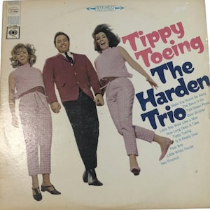 May include: A vintage vinyl record album cover featuring a trio of singers, two women and one man, dressed in pink and white checkered outfits. The album title is "Tippy Toeing The Harden Trio" with a list of songs on the back cover.