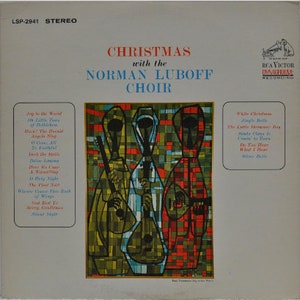 Puede incluir: Una portada de álbum de vinilo vintage con una ilustración colorida de estilo vitral de tres figuras que sostienen instrumentos musicales. El título del álbum es "Christmas with the Norman Luboff Choir" y la discográfica es "RCA Victor Dynagroove Recordings".