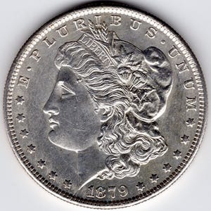 Könnte beinhalten: Eine silberne Morgan-Dollar-Münze mit dem Jahr 1879 auf der Unterseite. Die Münze zeigt ein Profil von Lady Liberty mit der Inschrift "E PLURIBUS UNUM" am oberen Rand.