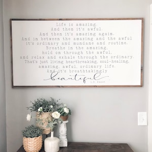 May include: A wooden sign with a white background and black text that reads "Life is amazing. And then it's awful. And then it's amazing again. And in between the amazing and the awful it's ordinary and mundane and routine. Breathe in the amazing, hold on through the awful, and relax and exhale through the ordinary. That's just living heartbreaking, soul-healing, amazing, awful, ordinary life. And it's breathtakingly beautiful. L.R. Knost"