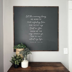 May include: A dark gray wooden sign with white lettering that reads "let the morning bring me word of your unfailing love. For I've put my trust in You. Show me the way I should go. For to You I entrust my life. Psalm 143:8"