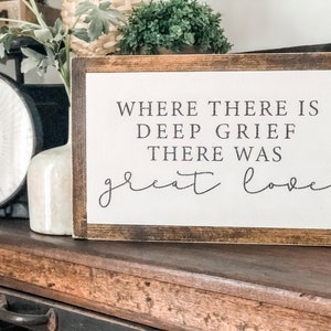 May include: A wooden sign with a white background and black text that reads "Where there is deep grief there was great love".