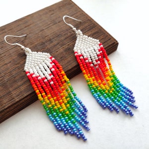May include: A pair of long, rainbow-colored beaded earrings with silver hooks. The earrings are made of small, round beads in shades of white, red, orange, yellow, green, blue, and purple.
