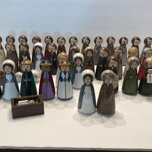 May include: A set of 30 hand-painted ceramic figurines depicting the Nativity scene. The figures are all different sizes and are painted in various colors, including white, brown, blue, green, and red. The figures are arranged in a circle around a small wooden manger.