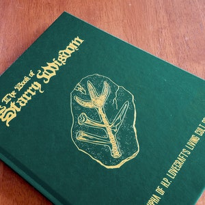 May include: A green hardcover book with gold lettering titled "The Book of Starry Wisdom" and a gold illustration of a fossil on the front cover. The bottom of the cover reads "Cthulhu of H.P. Lovecraft's Living Cult of Cthulhu."
