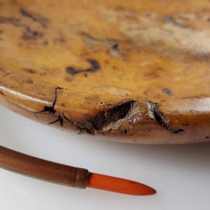 May include: A wooden bowl with a natural wood grain finish and a copper-colored metal handle. The bowl has a crack on the side and is slightly chipped.