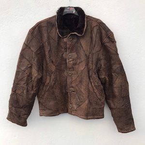 May include: A brown leather jacket with a patchwork design. The jacket has a fur-lined collar and a button closure.