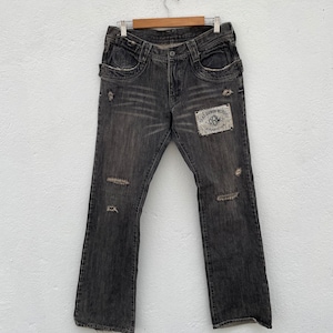 Op de afbeelding: Gestoorde zwarte denim jeans met een klein patch op het rechterbeen met de tekst "Gear Baron Motors" en een logo.