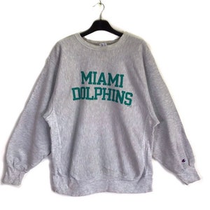 Puede incluir: Una sudadera gris Champion con las palabras "Miami Dolphins" en letras verdes en la parte delantera.