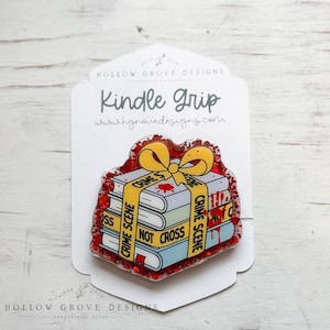 Puede incluir: Un agarre para Kindle con una pila de libros con las palabras "Crime Scene" y "Not Cross" en cinta amarilla. Los libros tienen salpicaduras de sangre roja y un lazo amarillo. El agarre está rodeado de purpurina roja.