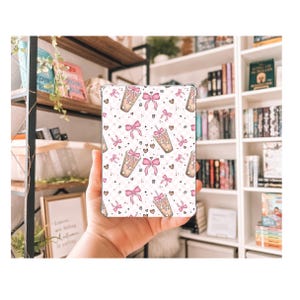 May include: A white and pink patterned phone case with a repeating design of pink bows and brown cups with pink straws and sprinkles.