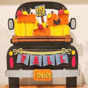 Peut inclure: Un camion en bois noir avec une benne pleine de citrouilles orange. Le camion a une pancarte qui dit "U-Pick 25c" et une bannière qui dit "FALL". Le camion a également une plaque d'immatriculation qui dit "Pumpkins".