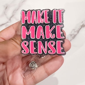 以下が含まれることがあります： 「MAKE IT MAKE SENSE」の文字が白縁取りの明るいピンク色で、暗くキラキラした背景に配置された長方形のバッジリール。 バッジリールは透明なプラスチッククリップとシルバーの金属製リールを備えています。