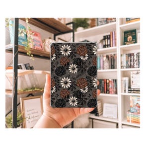 May include: A phone case with a floral pattern featuring brown, black, and white roses and daisies on a dark gray background.