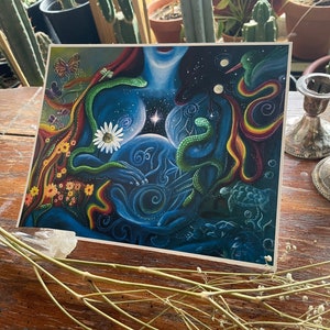 May include: A colorful abstract painting with a blue, green, and red color scheme. The painting features a woman's body with a snake wrapped around her, a hummingbird, and a daisy. The background is a dark blue with stars and swirls.