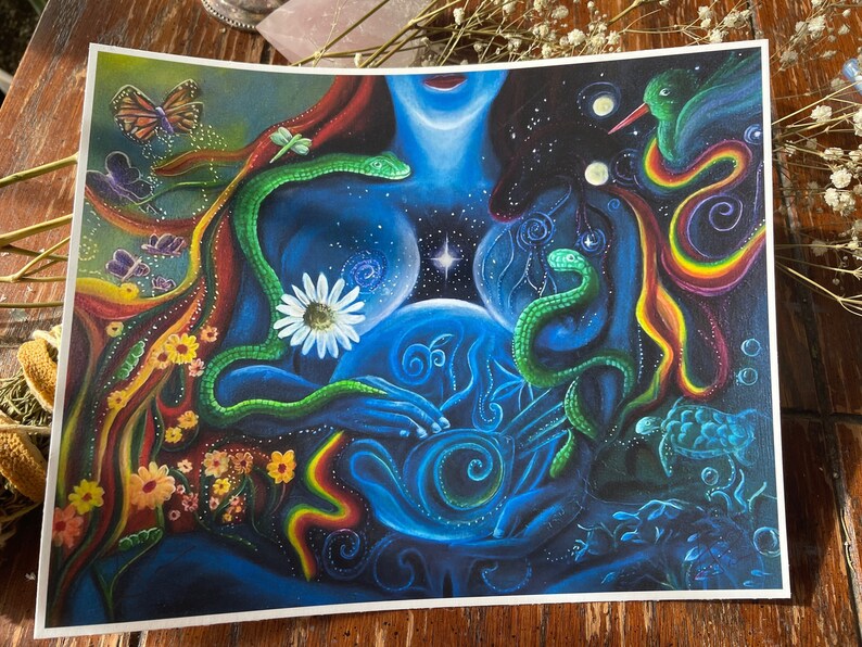 May include: A colorful painting depicting a woman with a glowing orb in her hands. The woman is surrounded by snakes, flowers, butterflies, and a hummingbird. The background is a dark blue with stars and swirls.