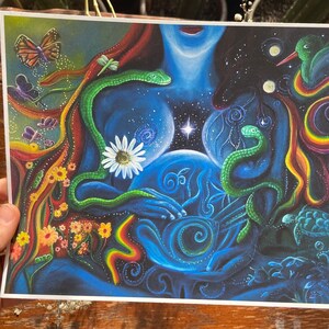 May include: A colorful, abstract painting depicting a woman with two snakes wrapped around her. The woman is holding a blue orb in her hands, and the background is filled with stars and other celestial imagery.