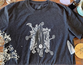 Könnte beinhalten: Ein dunkelgraues T-Shirt mit einem weißen Grafikdruck einer skelettartigen Figur, die von floralen Elementen umgeben ist. Die Grafik enthält die Zahl "5" in einem Kreis.