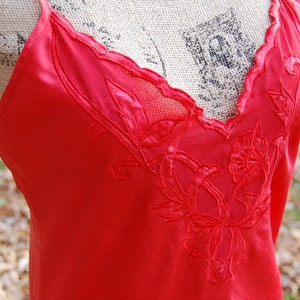 Puede incluir: Un camisón de satén rojo con un delicado bordado floral. El bordado es de un tono rojo más oscuro y presenta un patrón floral.