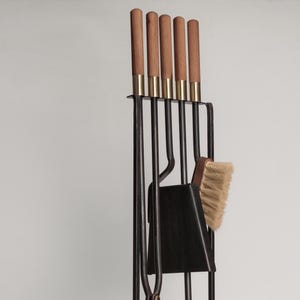 May include: A black metal fireplace tool set with wooden handles. The set includes a poker, tongs, shovel, and brush. The tools are mounted on a black metal stand.
