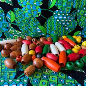 May include: A collection of wooden beads in various colors, including red, orange, yellow, green, white, and brown. The beads are oval-shaped and have a hole in the center. They are arranged on a colorful fabric background.