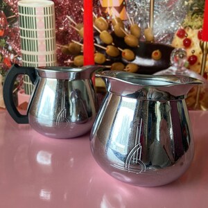 May include: Two silver creamer and sugar sets with a geometric design on a pink surface.