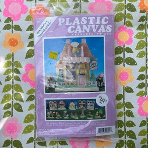 Puede incluir: Un kit de punto de aguja de lona de plástico con un edificio de panadería con un panadero oso de peluche. El kit incluye hilo acrílico, cabezas de madera, fieltro e instrucciones para hacer un proyecto. El tamaño terminado es de 15,24 cm x 17,78 cm. "Collect Them All" está impreso en el embalaje.