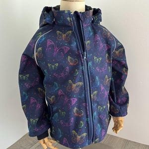 Könnte beinhalten: Eine dunkelblaue Kinderjacke mit Reißverschluss und einem bunten Schmetterlingsmuster. Die Jacke hat eine Kapuze und weiße Paspeln an den Rändern.