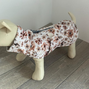 Könnte beinhalten: Ein Hundemantel mit einem Blumenmuster in Braun- und Weißtönen. Der Mantel hat eine Kapuze und einen Reißverschluss. Der Hundemantel ist für einen kleinen Hund konzipiert.