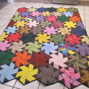 May include: A colourful quilt with a geometric pattern of pinwheels. The quilt is made of various fabrics in shades of red, orange, yellow, green, blue, purple, and brown. The pinwheels are outlined in black.
