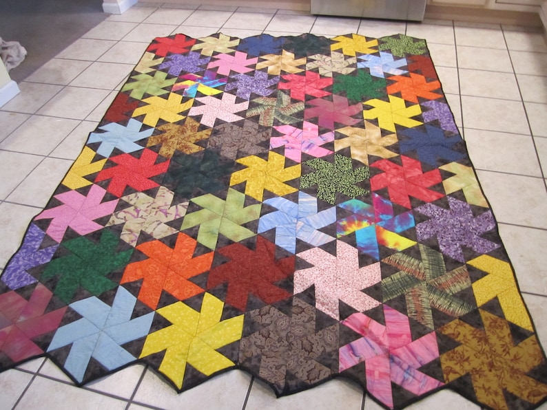 May include: A colourful quilt with a geometric pattern of pinwheels. The quilt is made of various fabrics in shades of red, orange, yellow, green, blue, purple, and brown. The pinwheels are outlined in black.