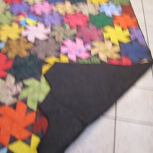 May include: A colourful patchwork quilt featuring a range of geometric shapes and patterns. The quilt is made from different fabrics in shades of red, green, blue, yellow and pink. The quilt is folded in half and the underside is black.