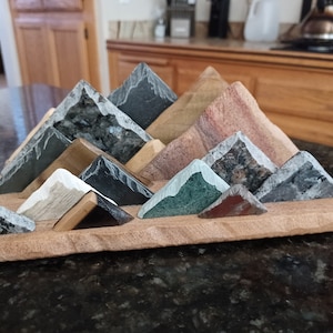 May include: A wooden base with a triangular arrangement of various colored and textured stone pieces, resembling a mountain range.