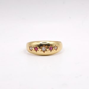May include: A gold band ring with five red and white gemstones set in a star shape.