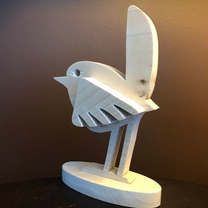 K&ouml;nnte beinhalten: Eine Holzskulptur eines Vogels mit langem Schwanz, Fl&uuml;geln und Beinen. Der Vogel steht auf einem kleinen ovalen Sockel.