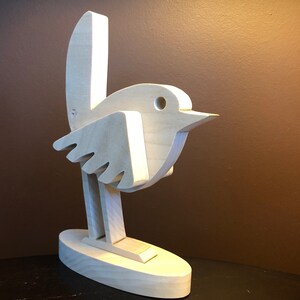 K&ouml;nnte beinhalten: Eine Holzskulptur eines Vogels mit einem einfachen, abstrakten Design. Der Vogel steht auf einem Sockel und hat einen langen, d&uuml;nnen Hals und einen kleinen Kopf mit einem Loch f&uuml;r ein Auge.