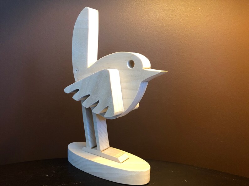 K&ouml;nnte beinhalten: Eine Holzskulptur eines Vogels mit einem einfachen, abstrakten Design. Der Vogel steht auf einem Sockel und hat einen langen, d&uuml;nnen Hals und einen kleinen Kopf mit einem Loch f&uuml;r ein Auge.