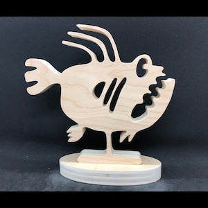 May include: A wooden sculpture of a cartoon fish with a large mouth and a stand. The fish is light brown and has a simple design.
