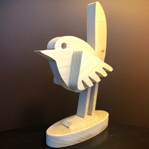 K&ouml;nnte beinhalten: Eine Holzskulptur eines Vogels mit einem einfachen, abstrakten Design. Der Vogel steht auf einem Sockel und hat einen langen, d&uuml;nnen Hals und einen kleinen Kopf. Die Skulptur ist aus hellem Holz gefertigt und hat eine nat&uuml;rliche Oberfl&auml;che.